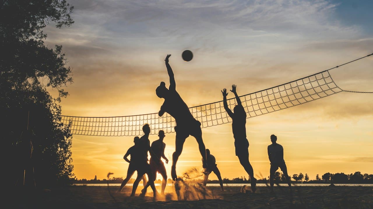 Gün batımında plaj voleybolu oynayanların silüeti