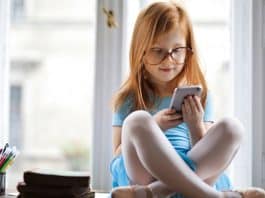 Çocukların dijital mahremiyeti açısından odasında akıllı telefonla sosyal medyaya bakan gözlüklü kız çocuğu
