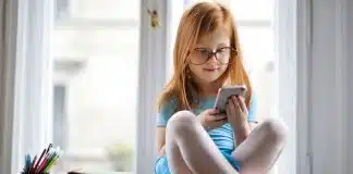Çocukların dijital mahremiyeti açısından odasında akıllı telefonla sosyal medyaya bakan gözlüklü kız çocuğu