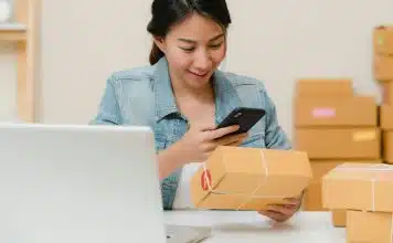 E-ihracat yapmadan önce bu 5 soruya cevap verin E-ihracat siparişlerini dizüstü bilgisayar ve kargo kutuları arasında telefondan kontrol eden bir kadın