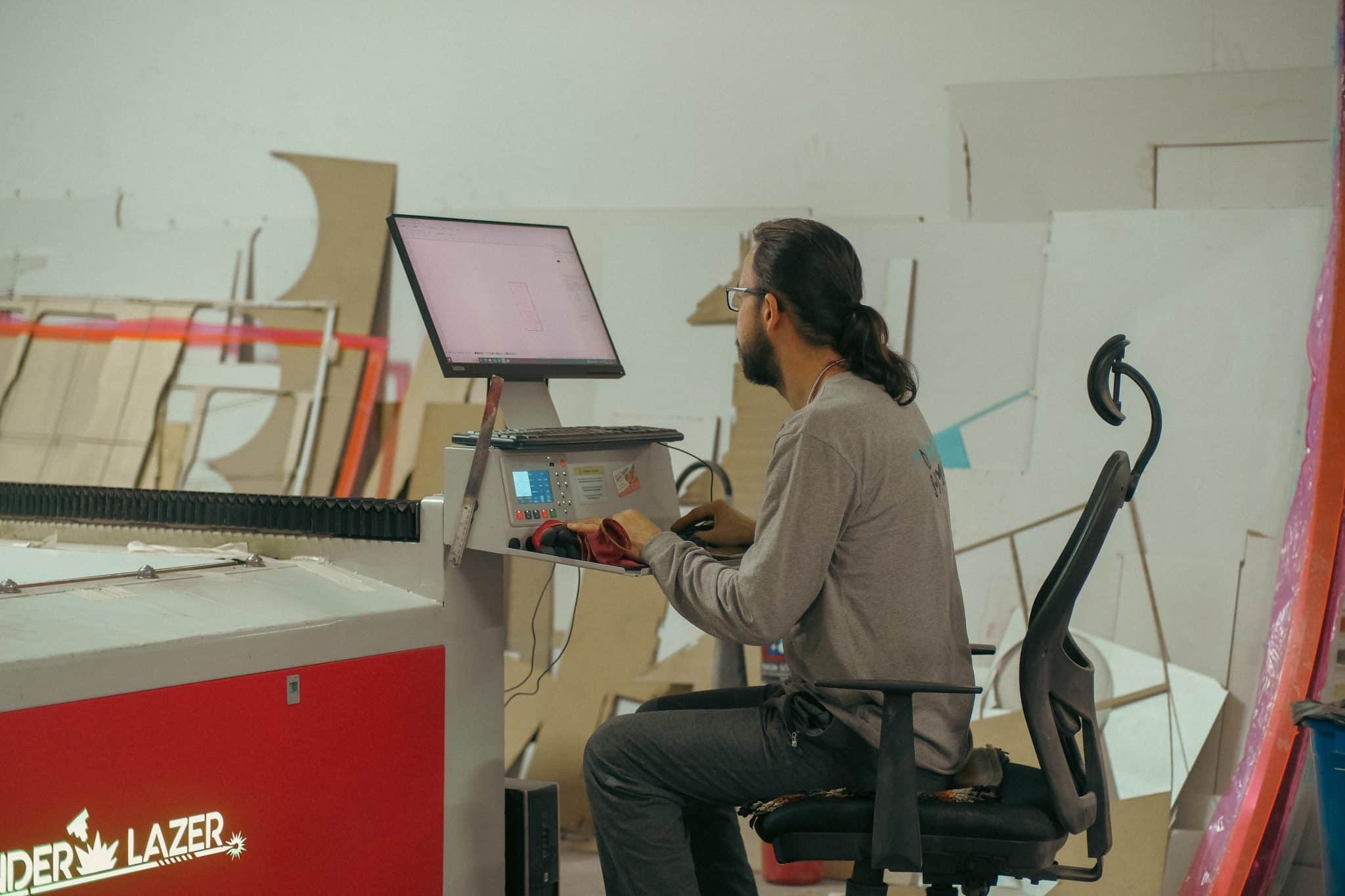 Üretim atölyesinde lazer kesim makinesinin bilgisayarında çalışan genç çalışan; e-ticarette rekabet genç kadrolarla hız kazanıyor