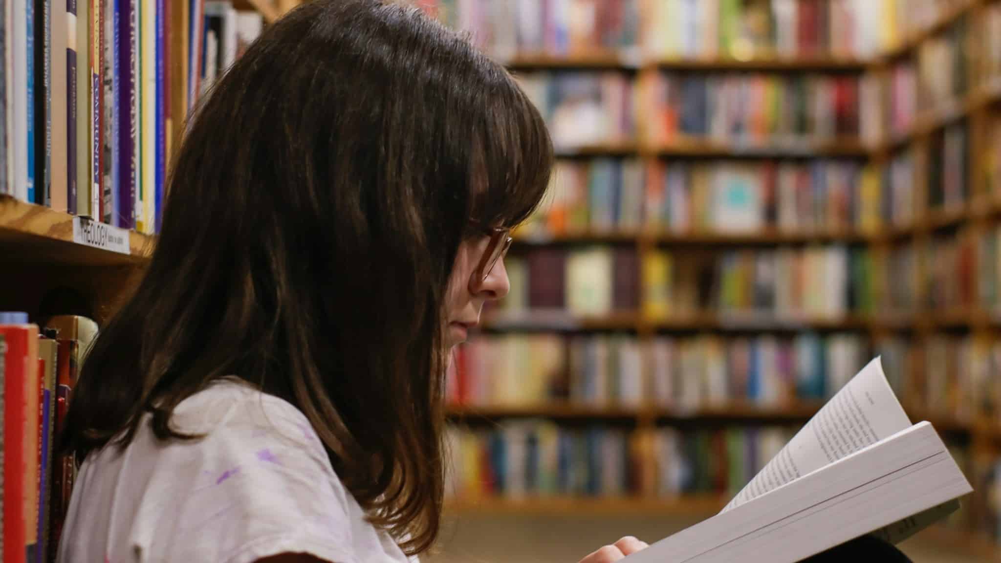 Kütüphanede kitap okuyan genç kadın; okuma kelime hazinesi için en güçlü kaynak