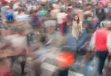 Toplumlar da çaresizliği öğreniyor: Kolektif öğrenilmiş çaresizlik nedir? Hareketli kalabalığın ortasında kıpırdamadan duran kadın; kolektif öğrenilmiş çaresizlik toplumsal pasifliği anlatıyor