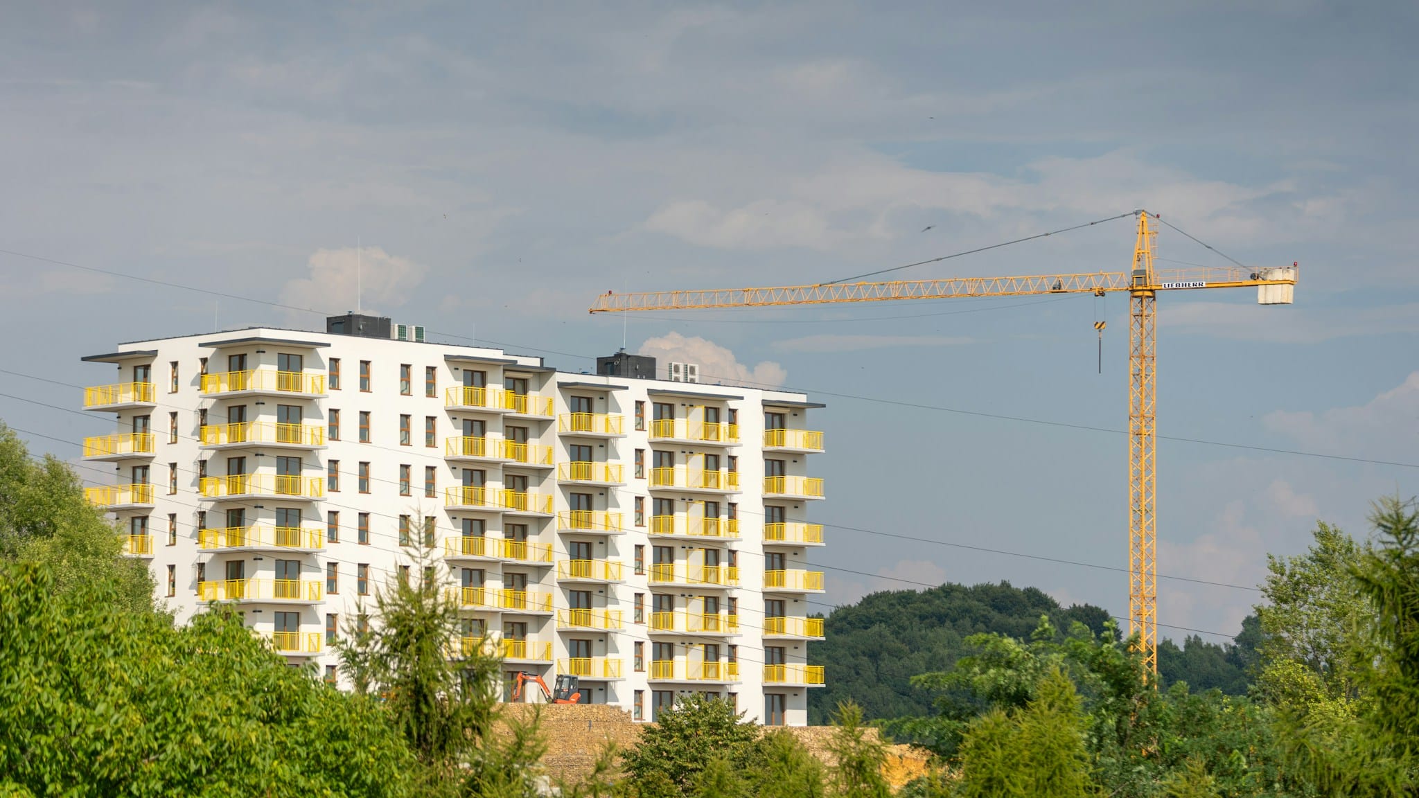 Yanında inşaat vinci bulunan sarı balkonlu yeni apartman; konut üretimi finansman, maliyet ve ruhsat engelleriyle karşı karşıya