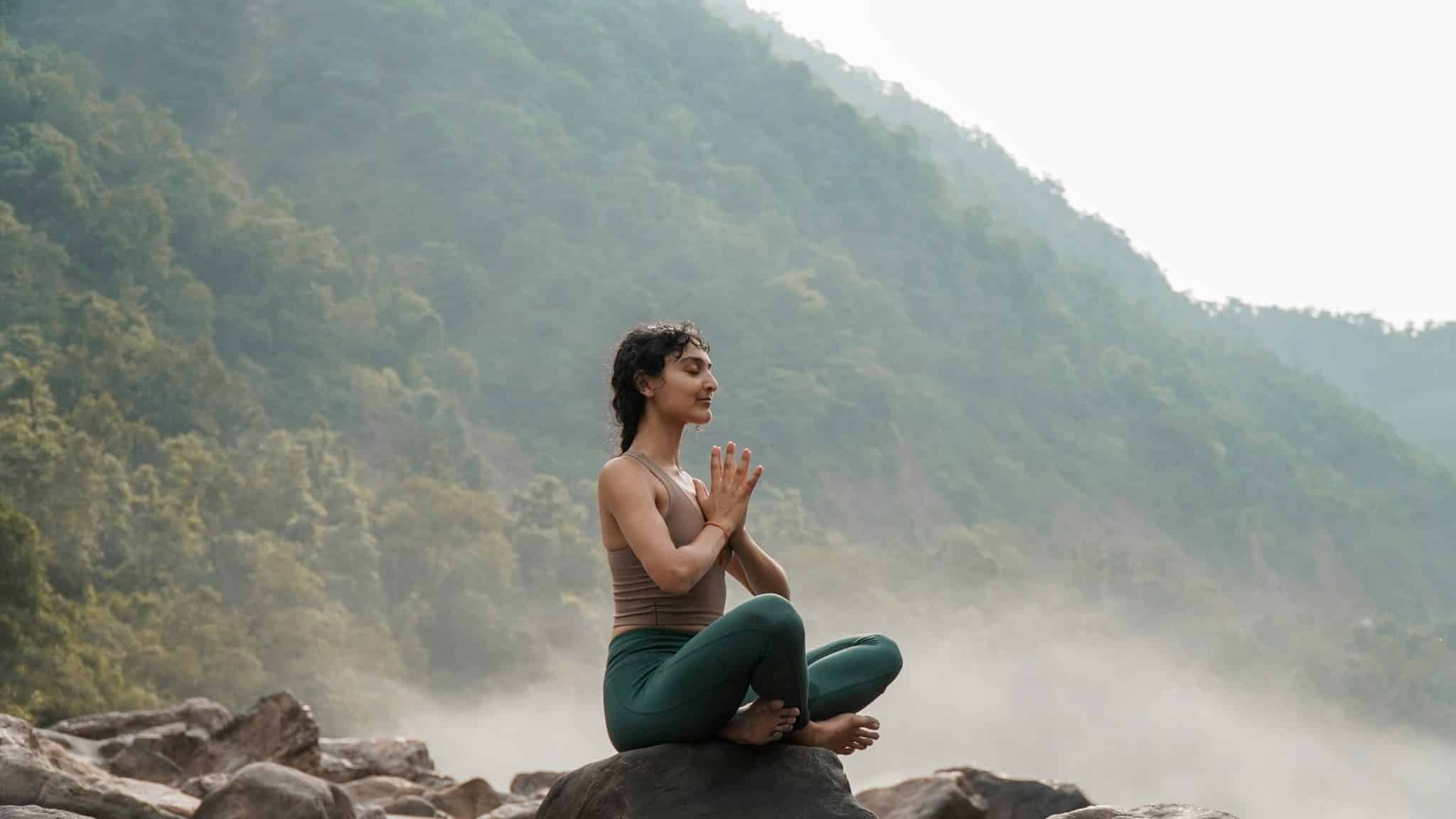 Doğada kayanın üzerinde meditasyon yapan kadın; manevi pratikler zihni şimdiye sabitliyor