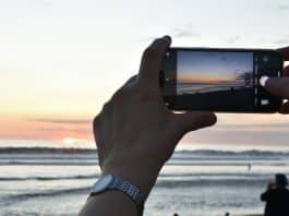 Mükemmel tatil karesini sosyal medyada paylaşmak için gün batımında plajda telefonla fotoğraf çeken eller