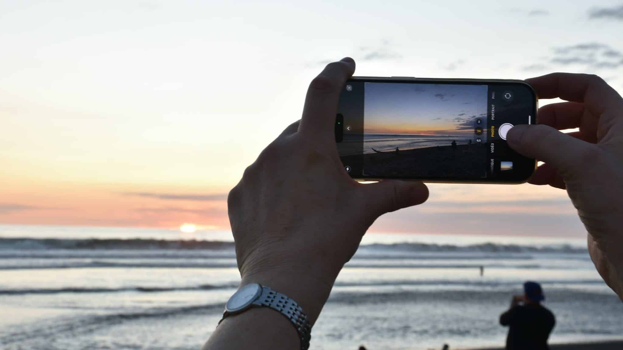 Mükemmel tatil karesini sosyal medyada paylaşmak için gün batımında plajda telefonla fotoğraf çeken eller
