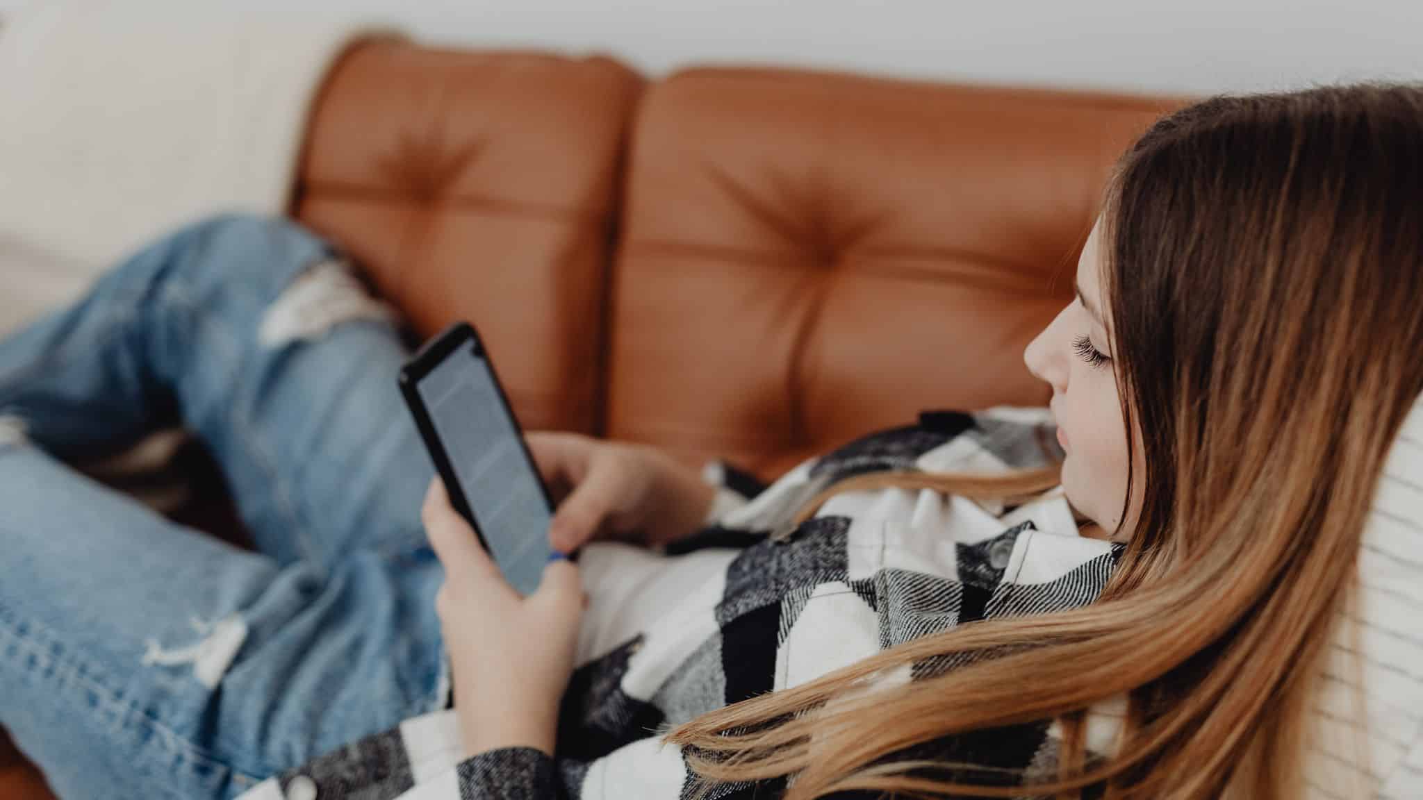 Sahte dinlenme örneği: Kanepede uzanıp akıllı telefonda sosyal medyada gezinen kadın