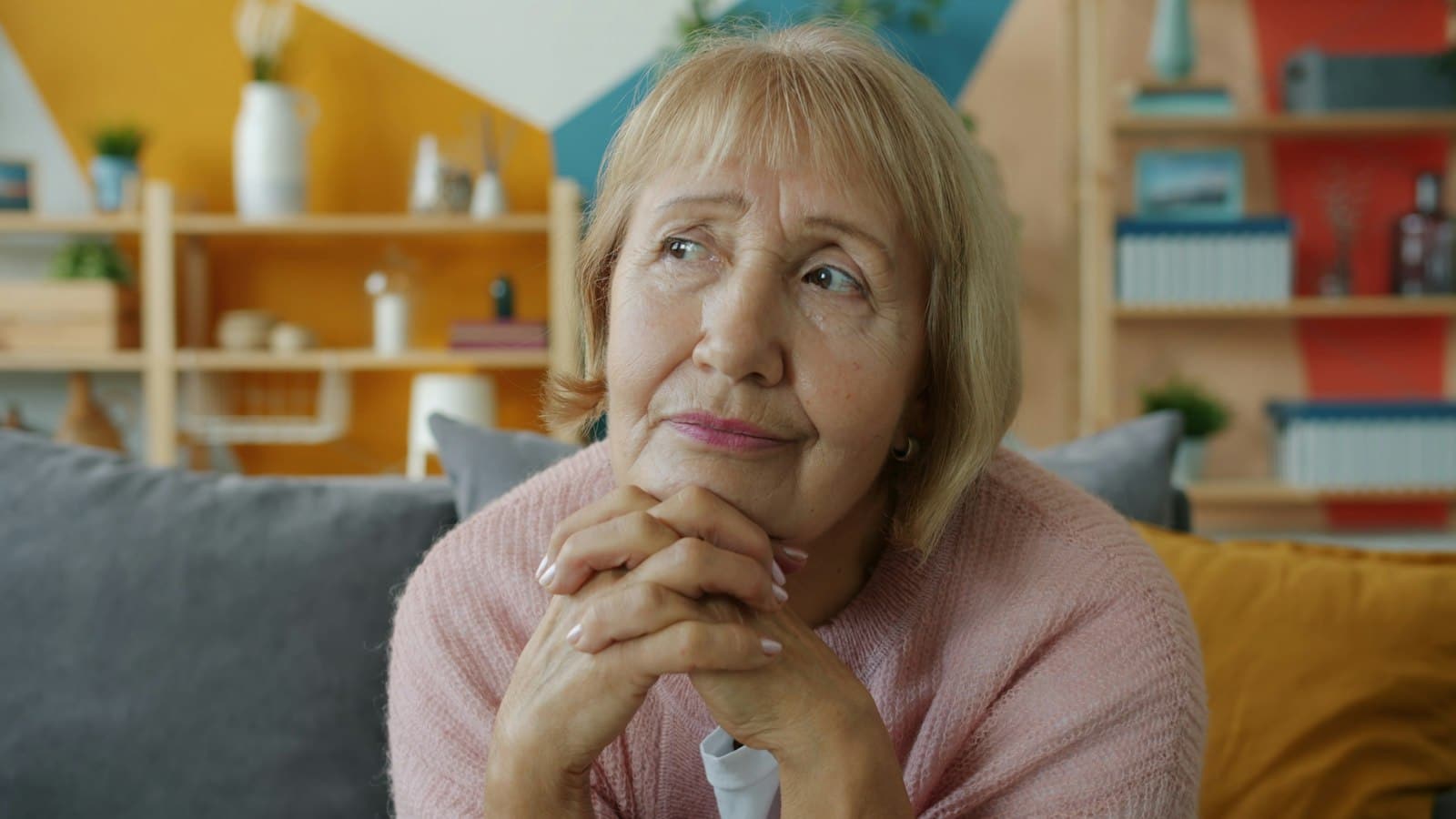 Unutkanlık ve Alzheimer endişesiyle evde koltukta ellerini kavuşturup düşünen yaşlı bir kadın